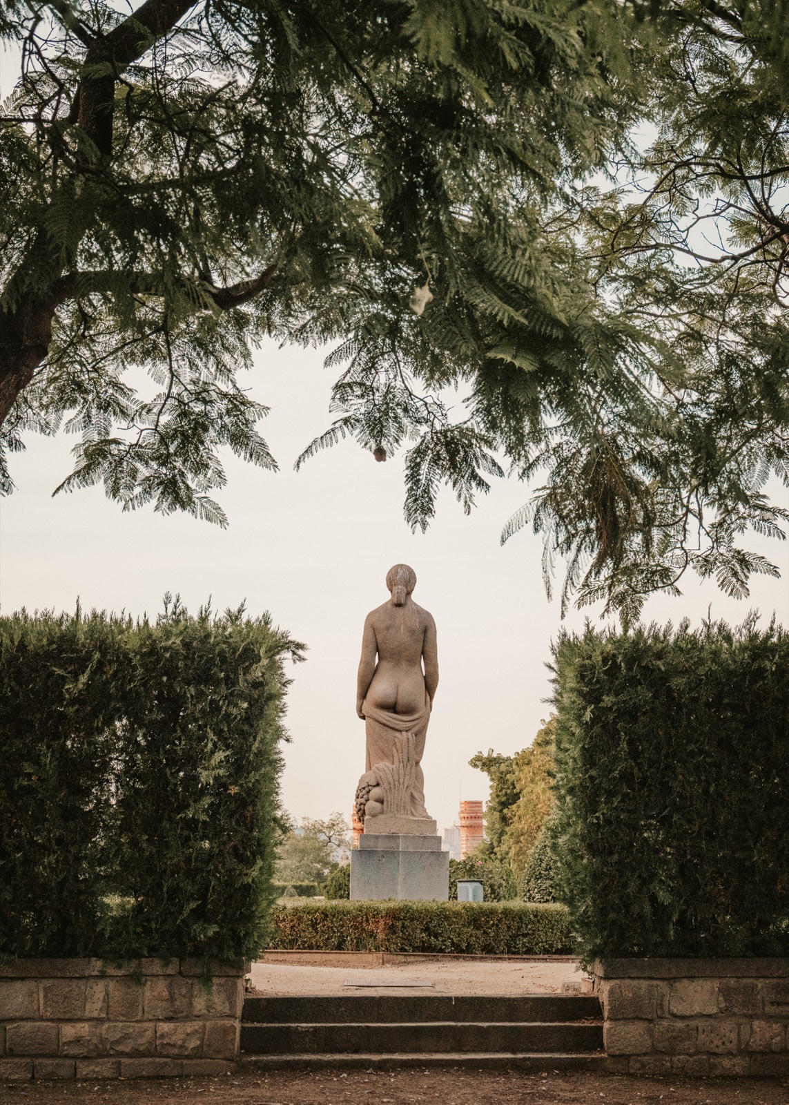 A stone statue in a garden, framed by hedges and branches