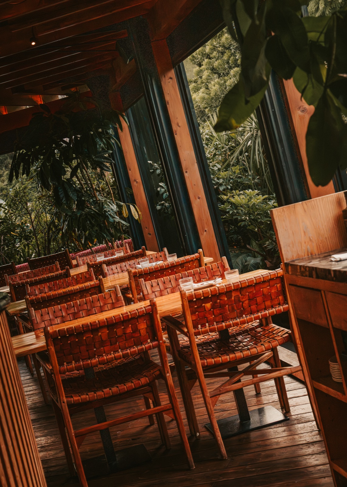 Woven chairs and tables on a wooden terrace, surrounded by greenery