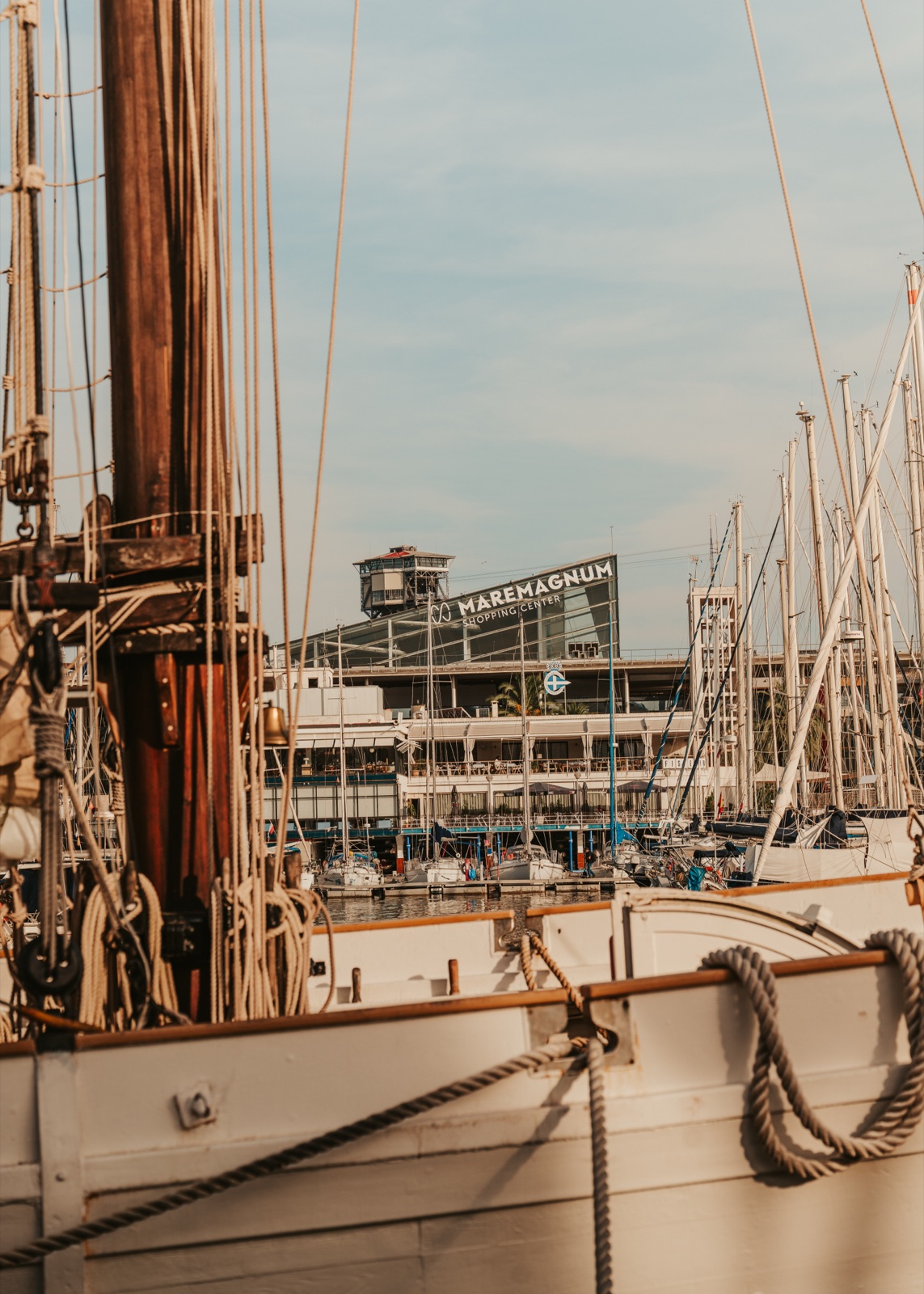 The mast and coiled ropes of a wooden sailing ship, with the Maremagnum beyond